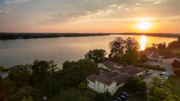 A lakeside property with a large house, a parking area, and a view of the sunset over the water.