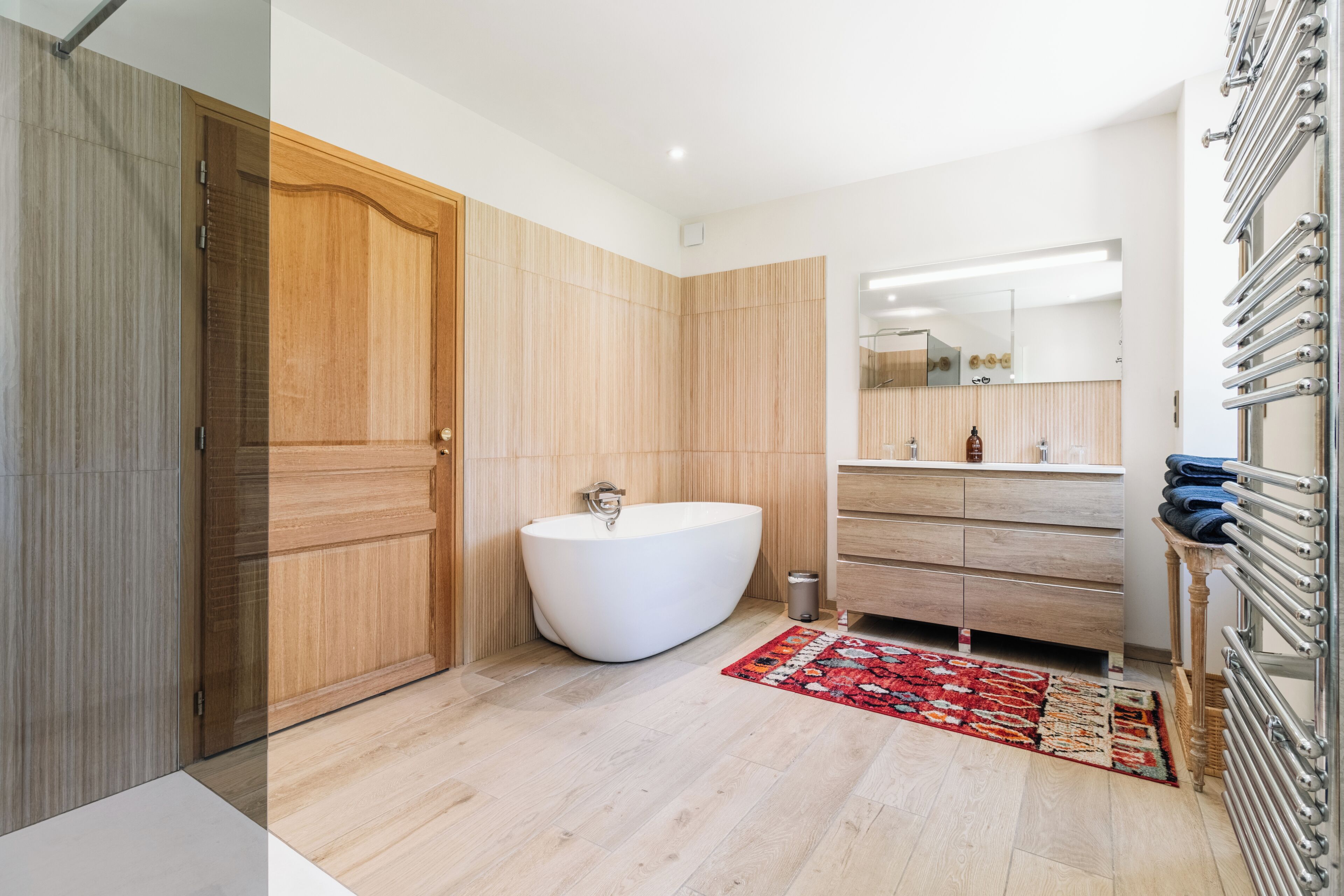 A modern bathroom with a freestanding bathtub, wooden panel walls, a large mirror, and a towel rack.