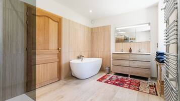 A modern bathroom with a freestanding bathtub, wooden panel walls, a large mirror, and a towel rack.