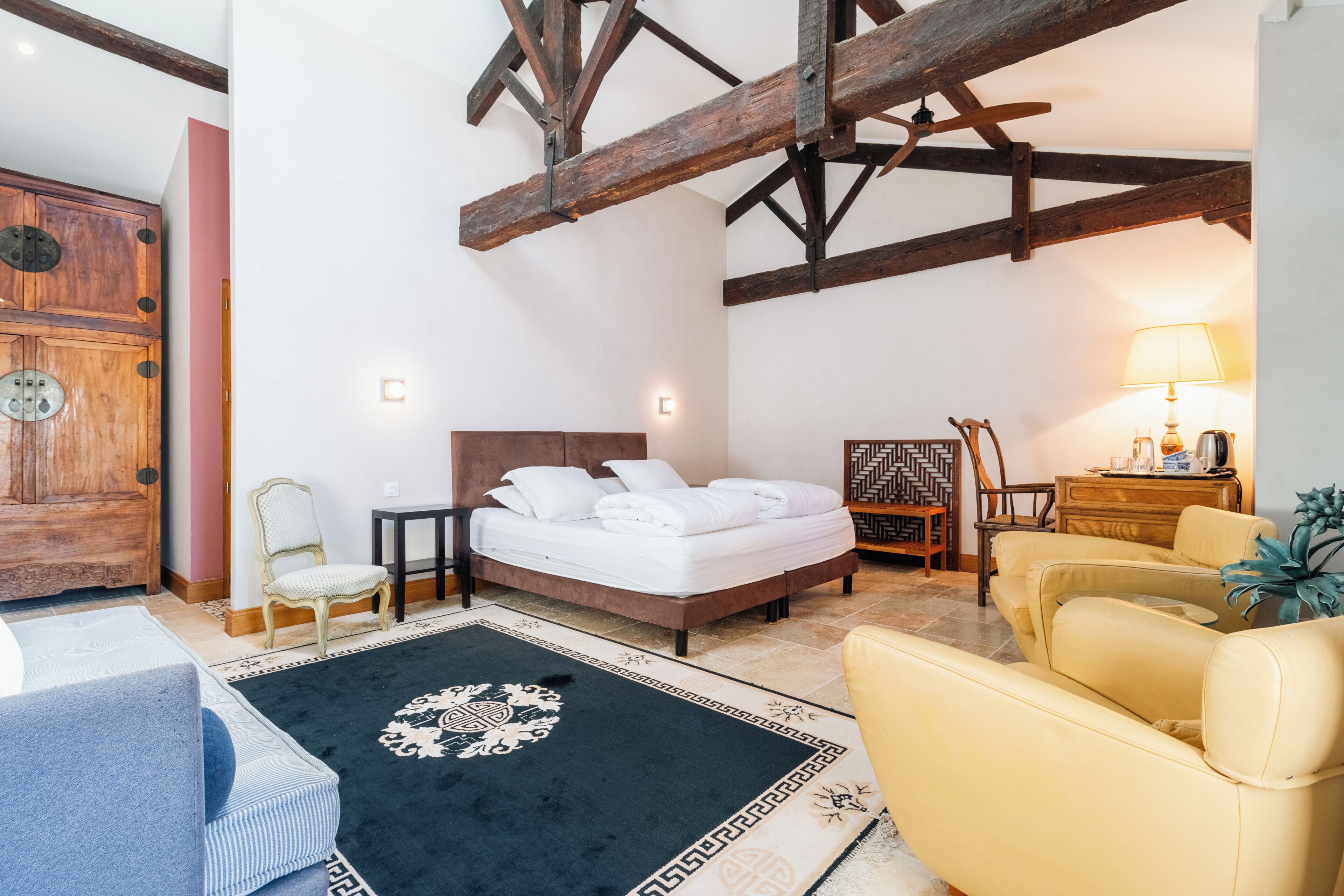 A room with a bed, a chair, a sofa, a wooden cabinet, and a lamp.