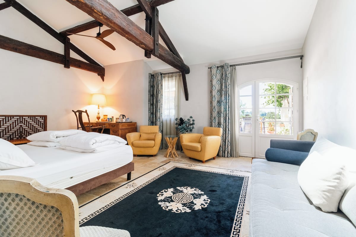 A bedroom with a bed, two armchairs, a small table, a lamp, and a window with curtains.