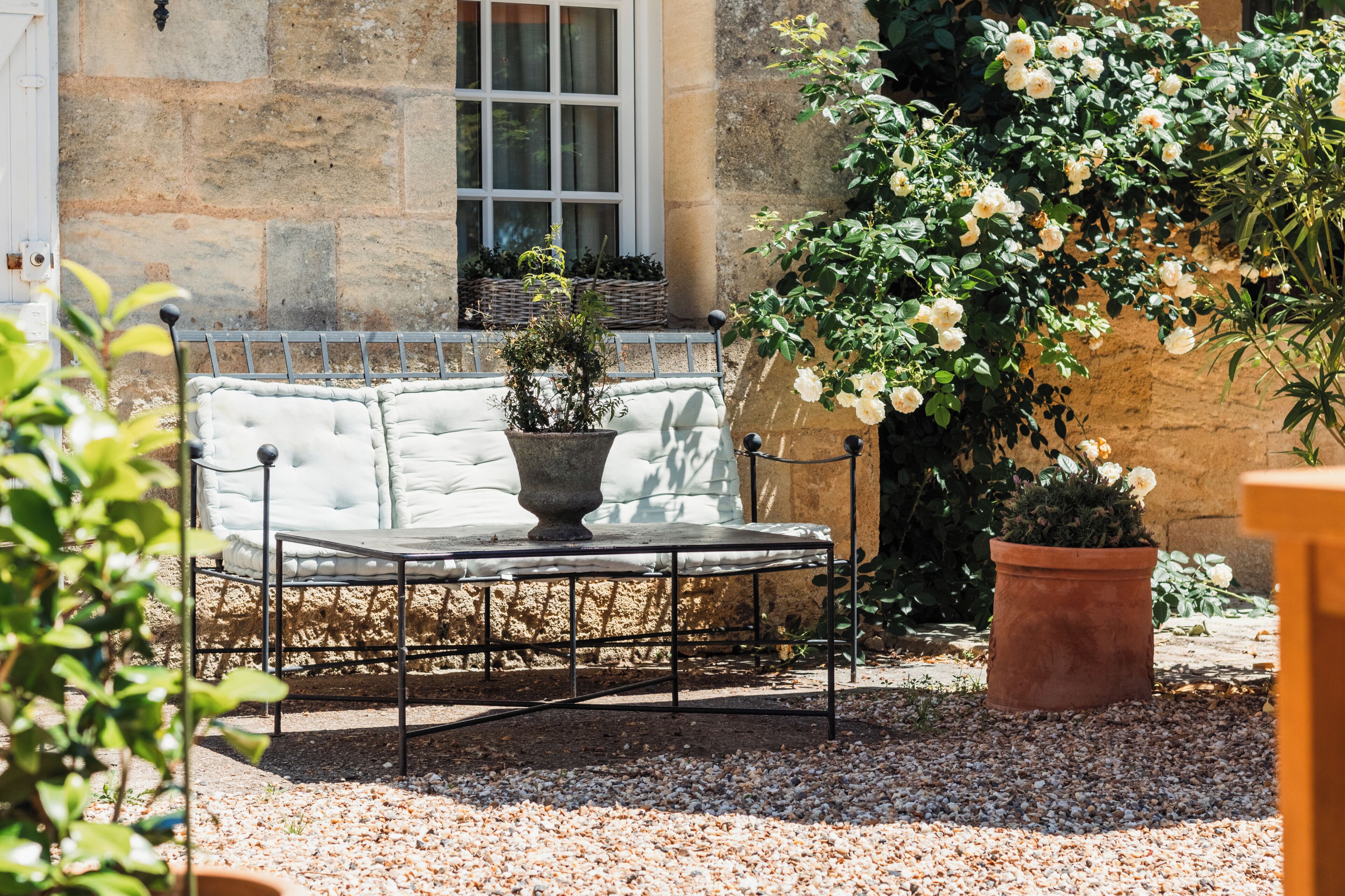 A stone building with a window, a metal bench with cushions, and potted plants.