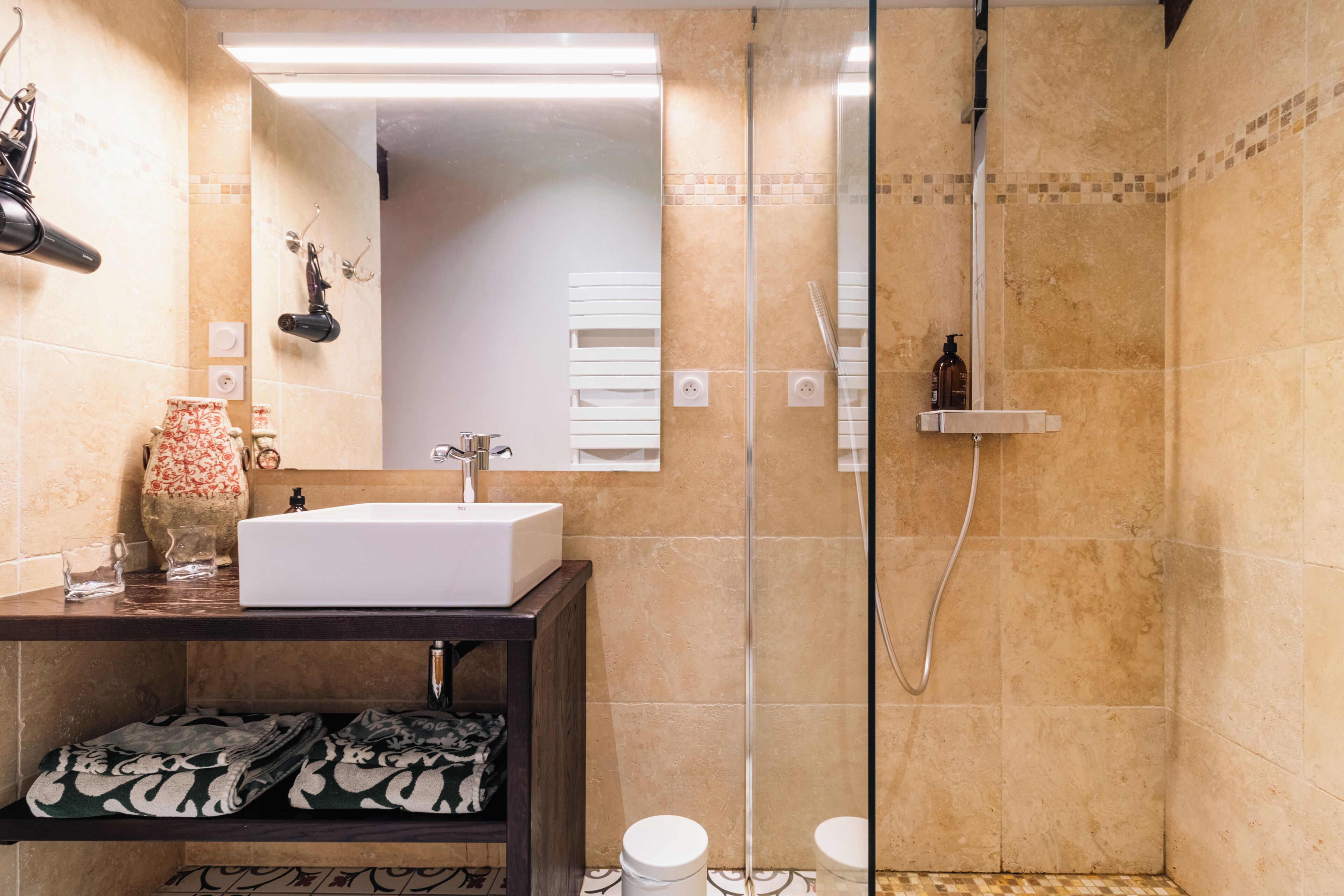 Un baño con un lavabo blanco, una cabina de ducha de vidrio y un espejo sobre el lavabo.