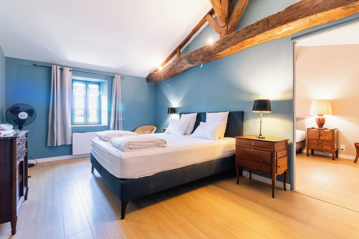 A bedroom with a bed, bedside tables, a dresser, a fan, and a window with curtains.