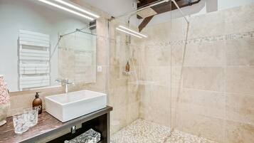 Een moderne badkamer met een grote spiegel, een witte wastafel, een douche en een betegelde vloer.