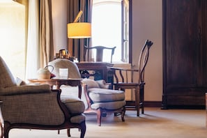 A room with a large window, a lamp, a wooden chair, a table, and a bookshelf.