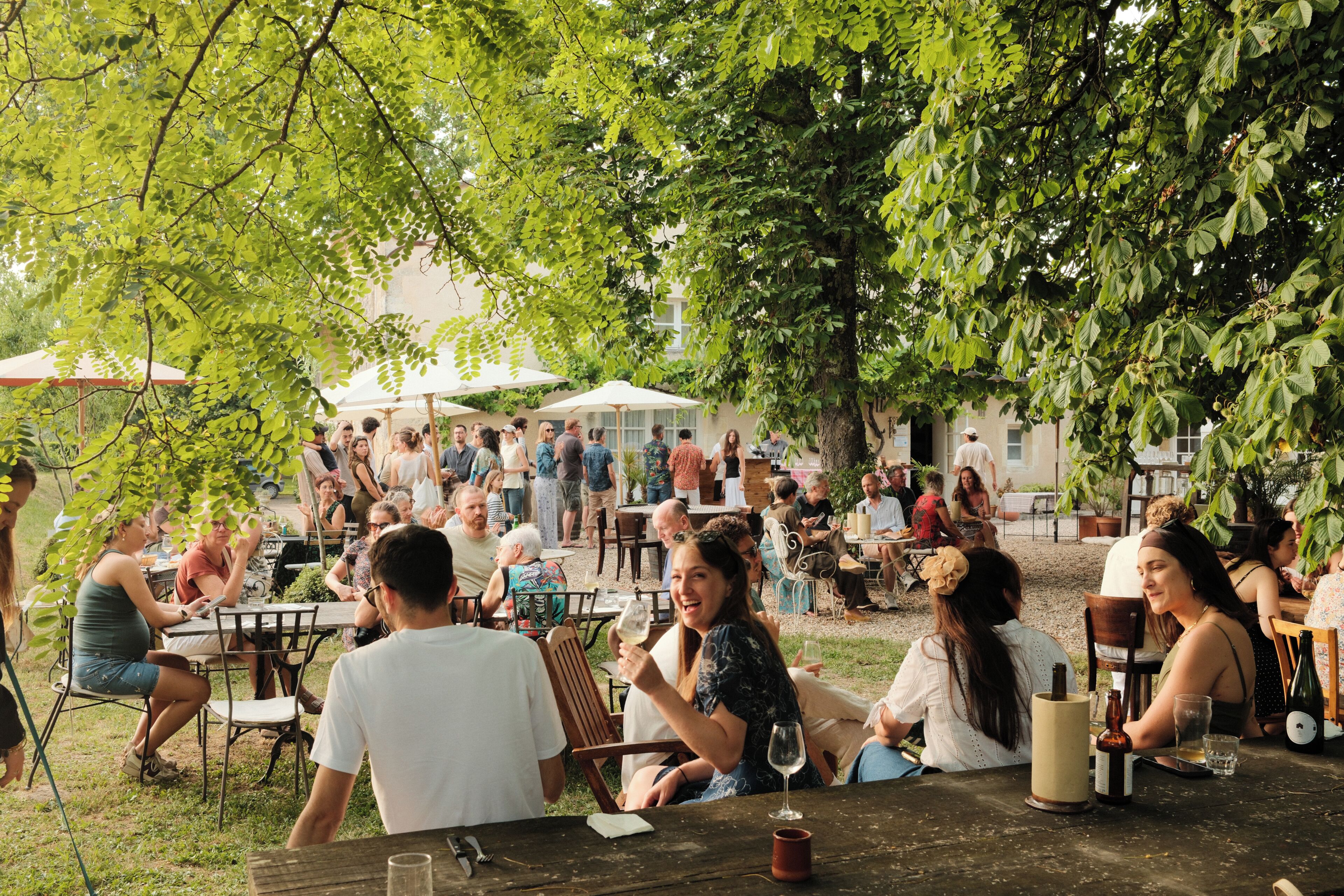 Une réunion en plein air où les participants sont assis à des tables sous les arbres.