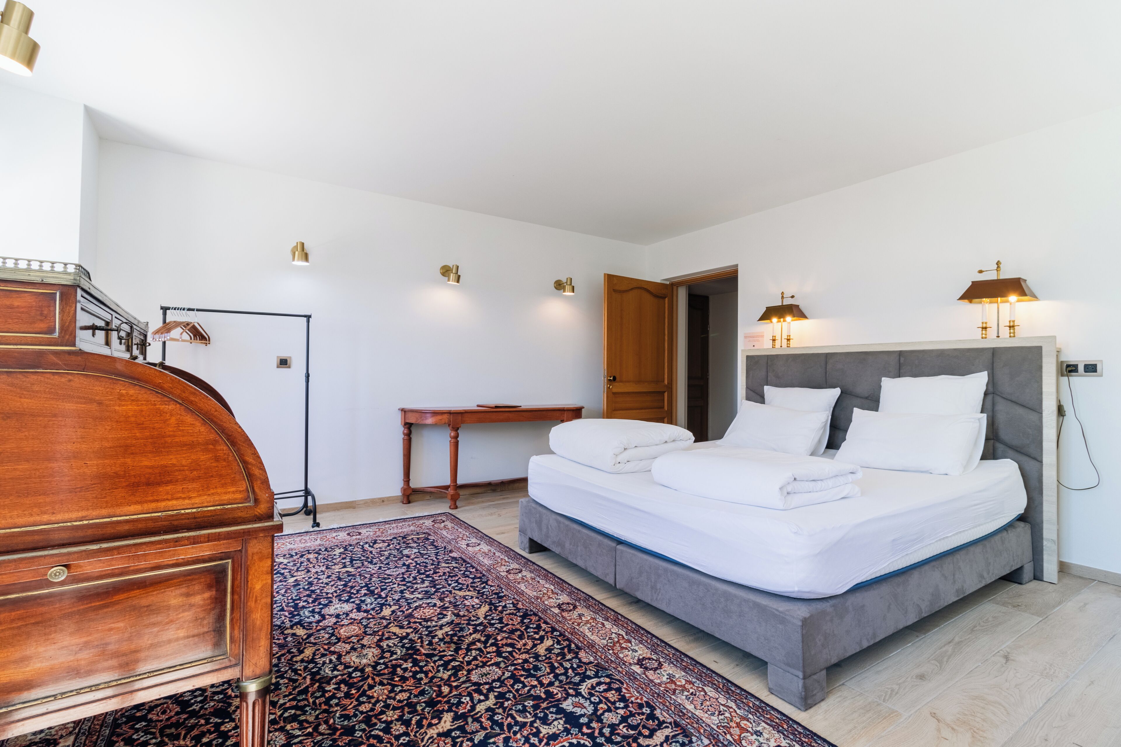 A bedroom with a bed, bedside table, lamp, and a wooden dresser.