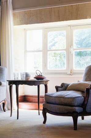 Una habitación con un ventanal grande, una mesa de madera con una cesta y dos sillones tapizados.