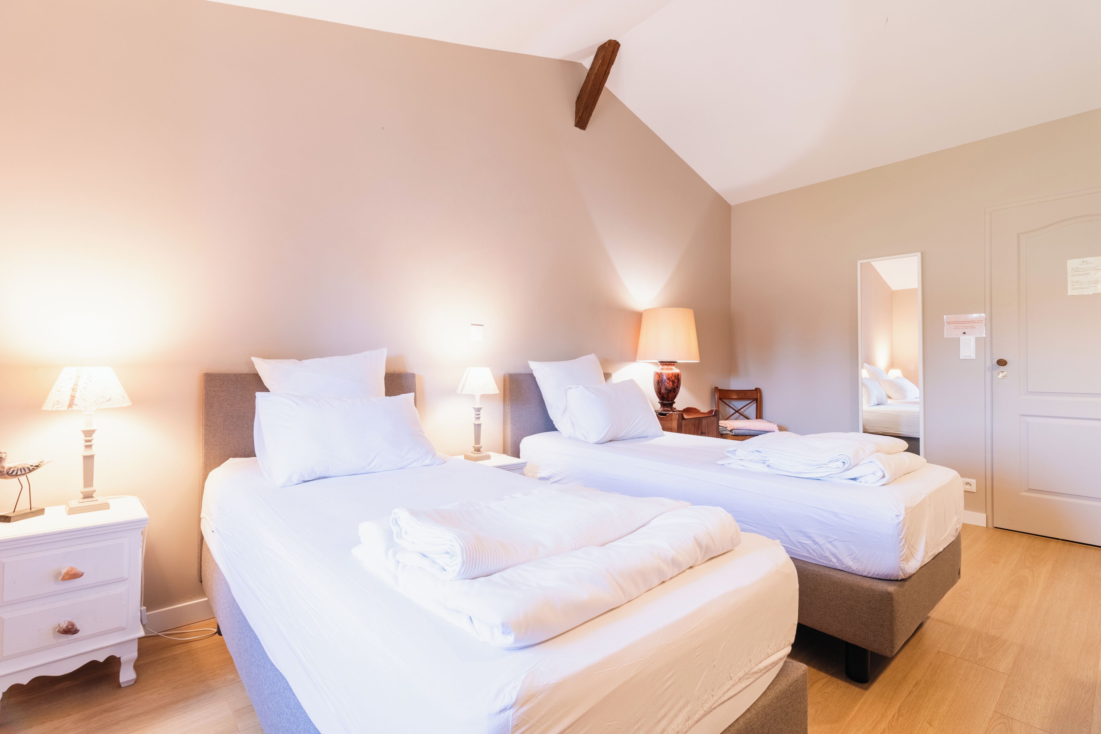 A hotel room with two beds, bedside lamps, a wooden headboard, a door, and a mirror.