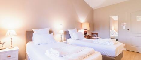 A hotel room with two beds, bedside lamps, a wooden headboard, a door, and a mirror.