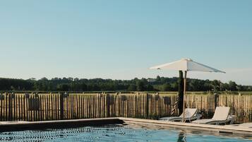 A clear blue swimming pool with two white lounge chairs and a white umbrella.