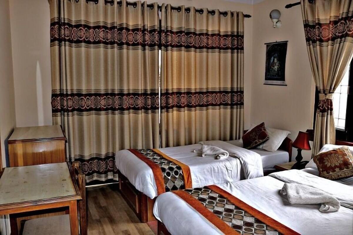 Habitación de hotel con dos camas, una mesa de madera y una lámpara fijada a la pared.