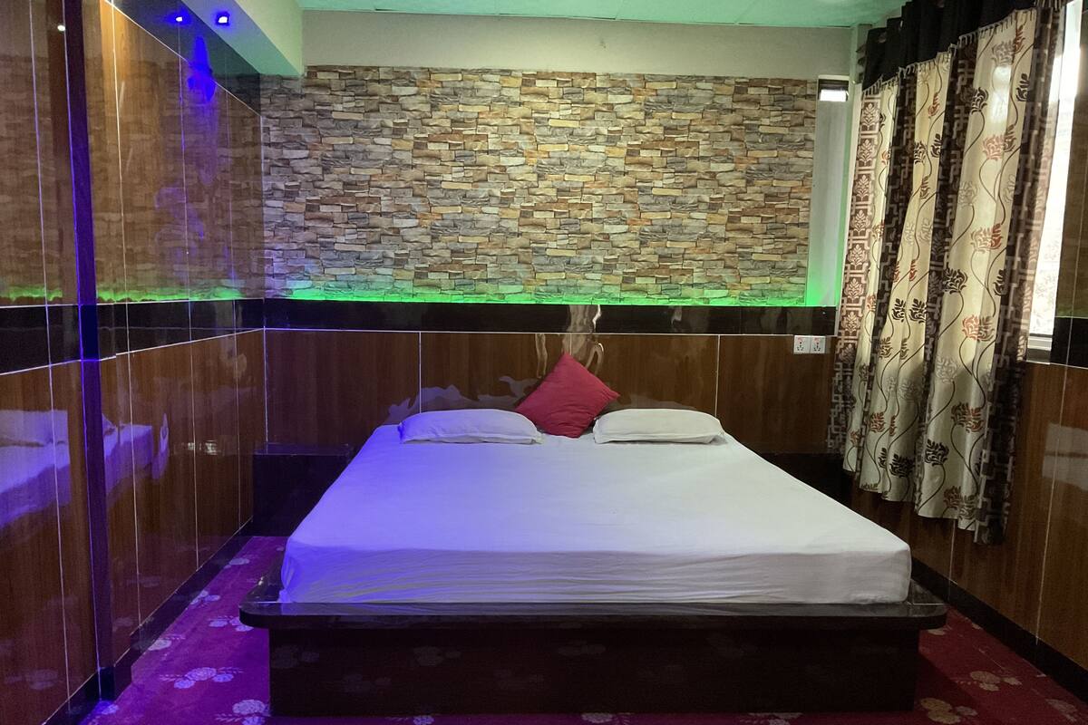 A room with a stone wall, a bed with white bedding, a red pillow, and a patterned carpet.