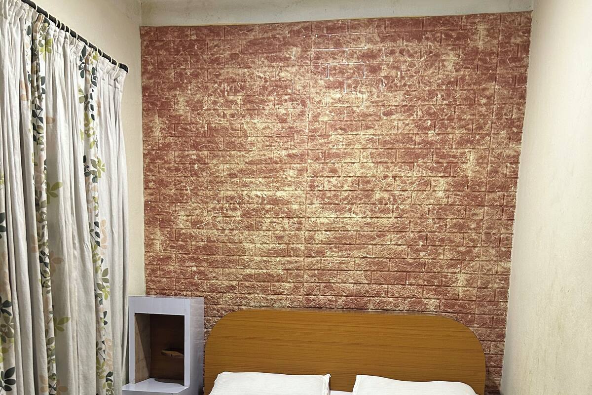 A bedroom with a brick-patterned headboard, a wooden bed frame, white bedding, and a small bedside table with a mirror.