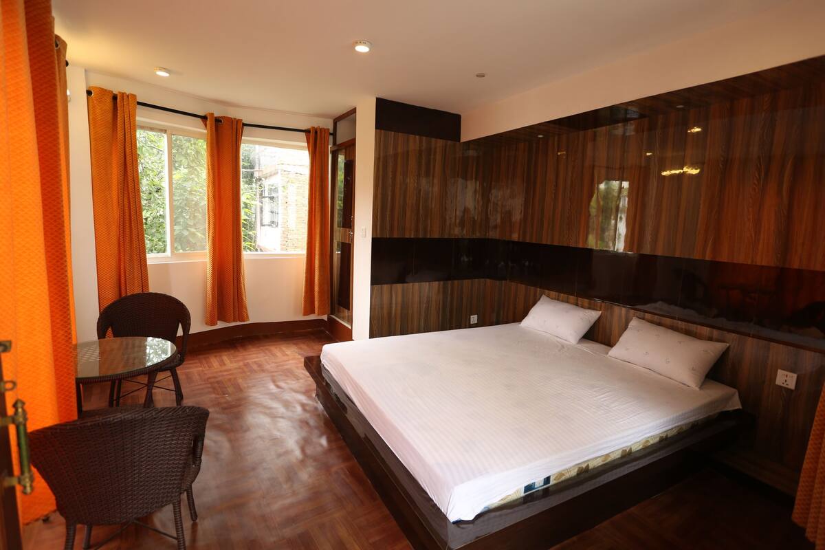 A hotel room with a large bed, a dining table, two chairs, and a window with curtains.
