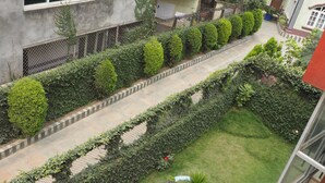 A courtyard with neatly trimmed hedges, a central planter with various plants, and a tiled pathway. - Sudha's Garden Home (Kathmandu)