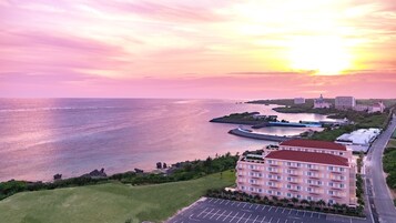 A coastal hotel with a parking lot, a view of the sea, and a road leading to the hotel.