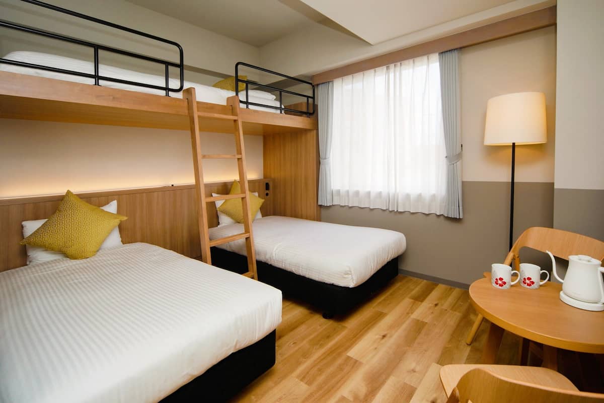 A hotel room with two beds, a wooden ladder, a table with two mugs, and a lamp.