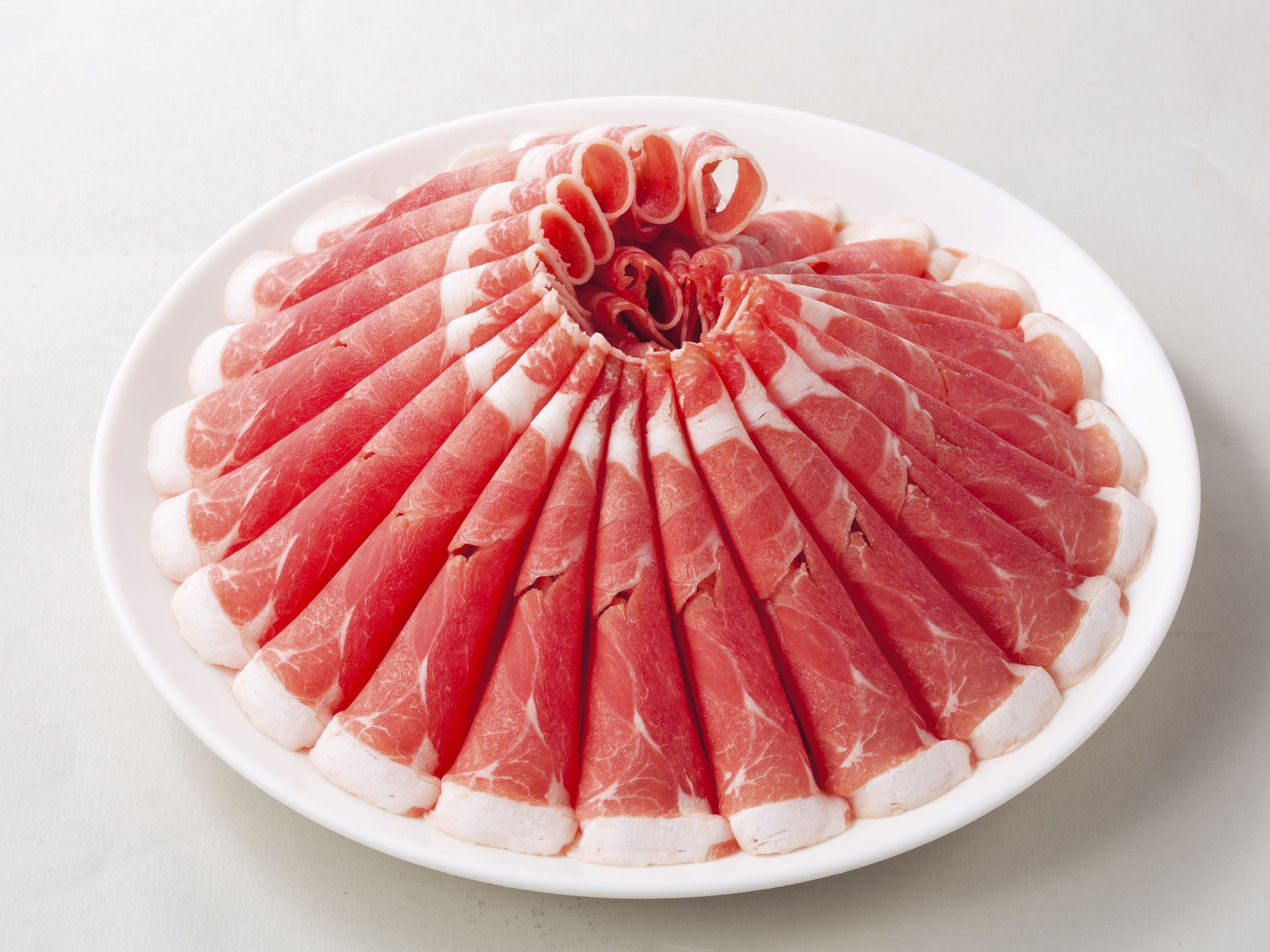 A plate of thinly sliced cured meat arranged in a fan shape on a white plate.