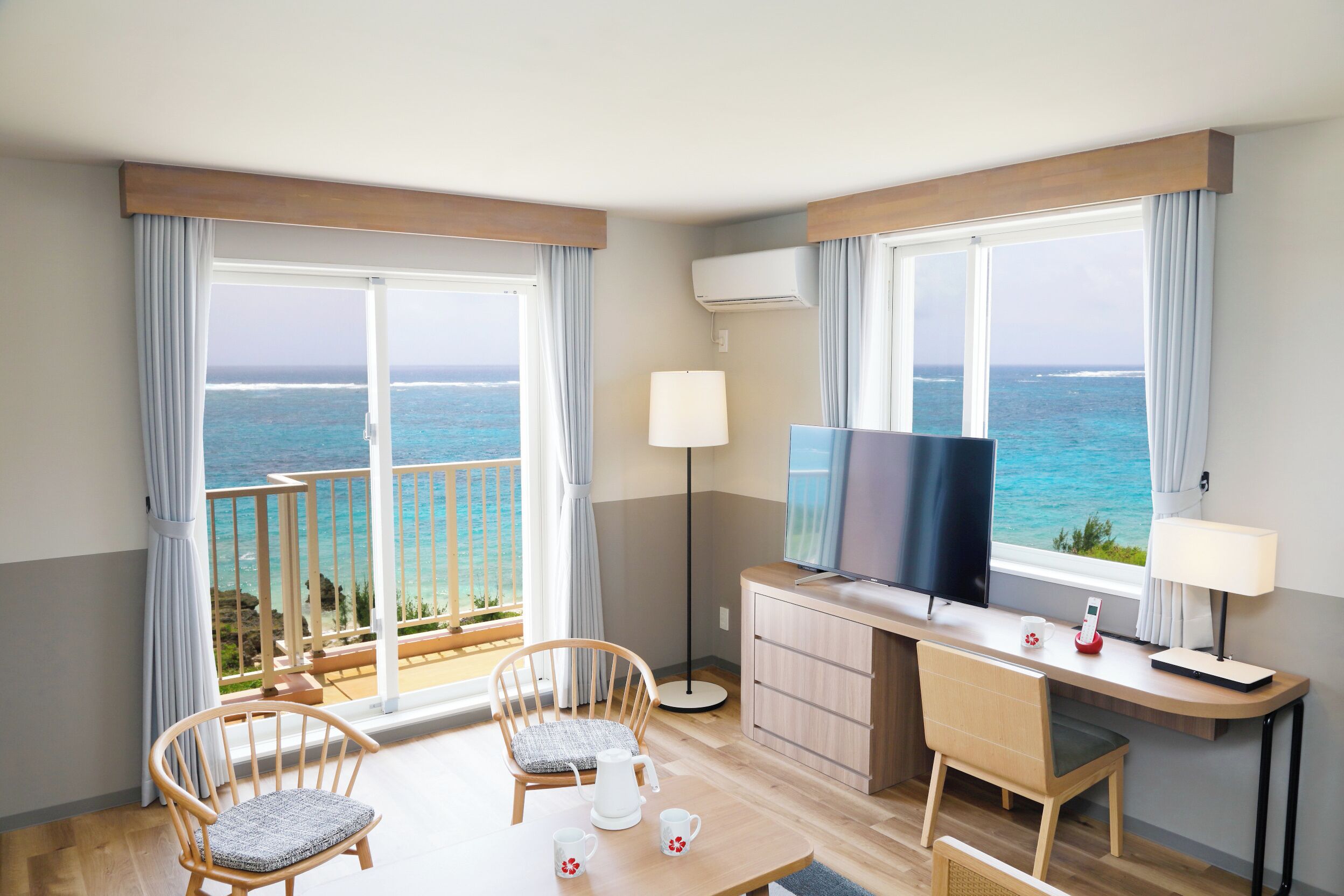 A hotel room with a balcony, a TV, a desk, and two chairs.