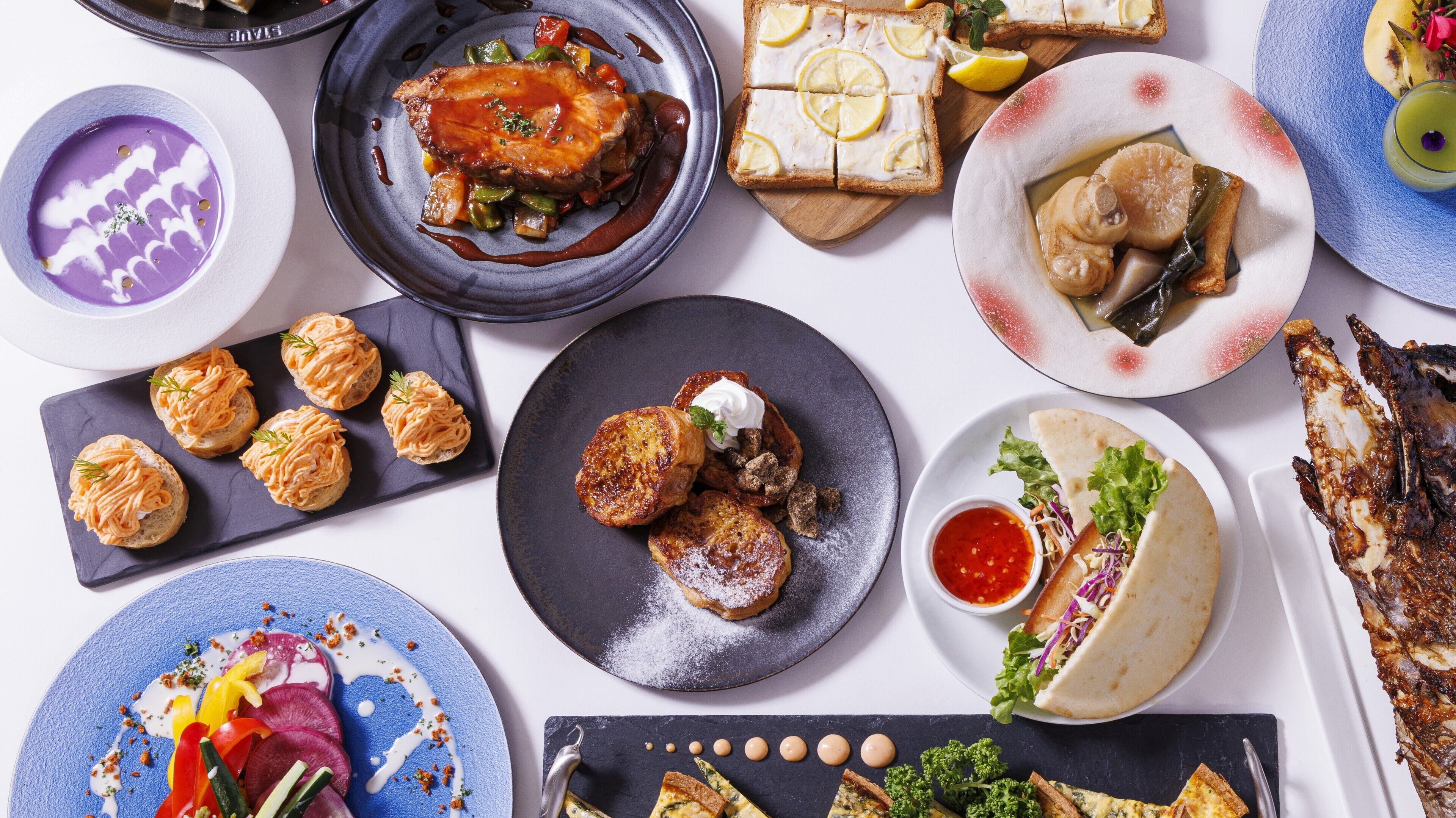 A variety of dishes including a plate of fish, bread with lemon slices, and a bowl of soup.