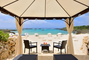 Un área de estar frente a la playa, con una mesa, dos sillas y un toldo con vistas al océano.