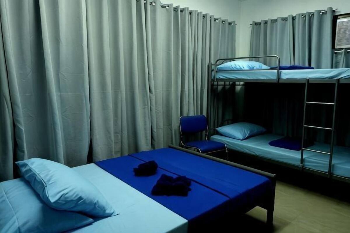 A dormitory room with bunk beds, a single bed, a chair, and curtains.