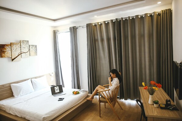 A hotel room with a bed, a desk, a laptop, a vase with flowers, and a wall art piece. - Red Hotel Da Nang (Da Nang)