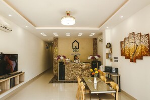 A hotel reception area with a marble counter, a reception desk, a television, and a dining area with chairs and a table. - Red Hotel Da Nang (Da Nang)