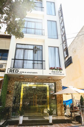 A hotel named RED HOTEL & APARTMENTS with a modern facade, large windows, and a visible outdoor seating area with umbrellas. - Red Hotel Da Nang (Da Nang)