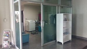 A room with a sliding glass door leading to a laundry area, a white shelving unit, and a cart with magazines. - J 168 Living (Bangkok)