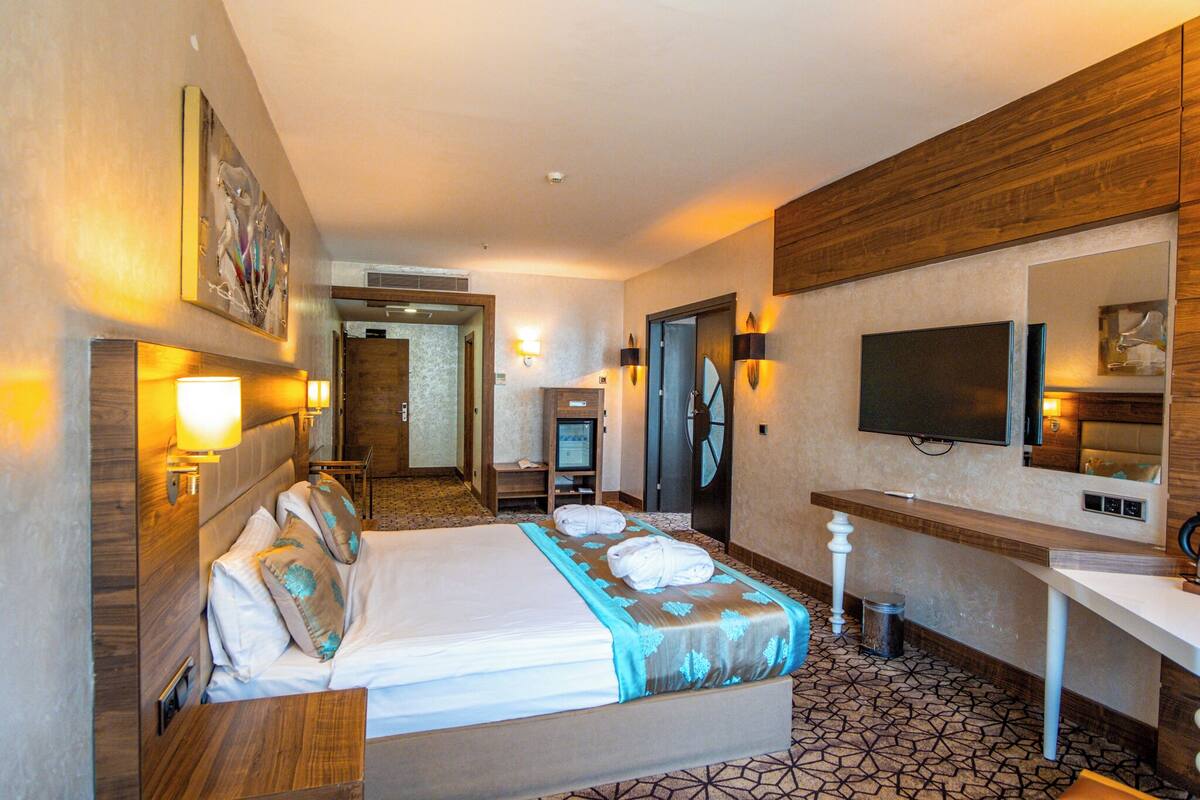 Ein Hotelzimmer mit Bett, Nachttisch, Fernseher und einem durchgegangenen Tür sichtbaren Badezimmer.