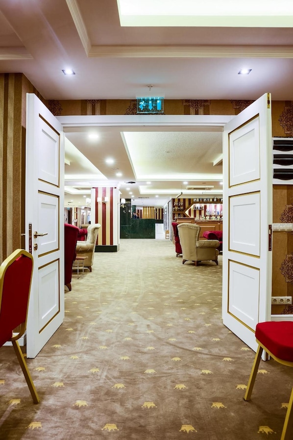 Un vestíbulo de hotel con puertas abiertas que dan a un bar, piso alfombrado y sillones tapizados en rojo.