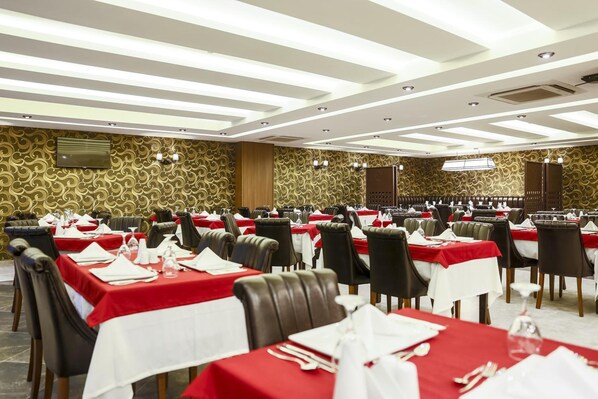 A large banquet hall with rows of tables set for dining, featuring red tablecloths and white napkins. - Inegol Royal Hotel (Inegol)