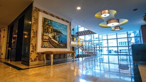 A spacious lobby with a marble floor, a large painting of a coastal scene, a bench, and a staircase leading to upper floors. - Inegol Royal Hotel (Inegol)