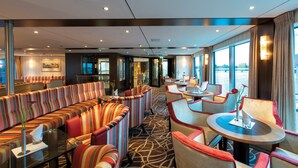 A modern hotel lobby with striped seating, round tables, and large windows offering views. - Crossgates Hotelship Messe - Köln (Cologne)