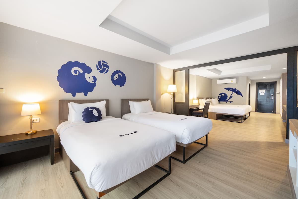 A modern hotel room with two beds, a nightstand, a lamp, and a large mirror.