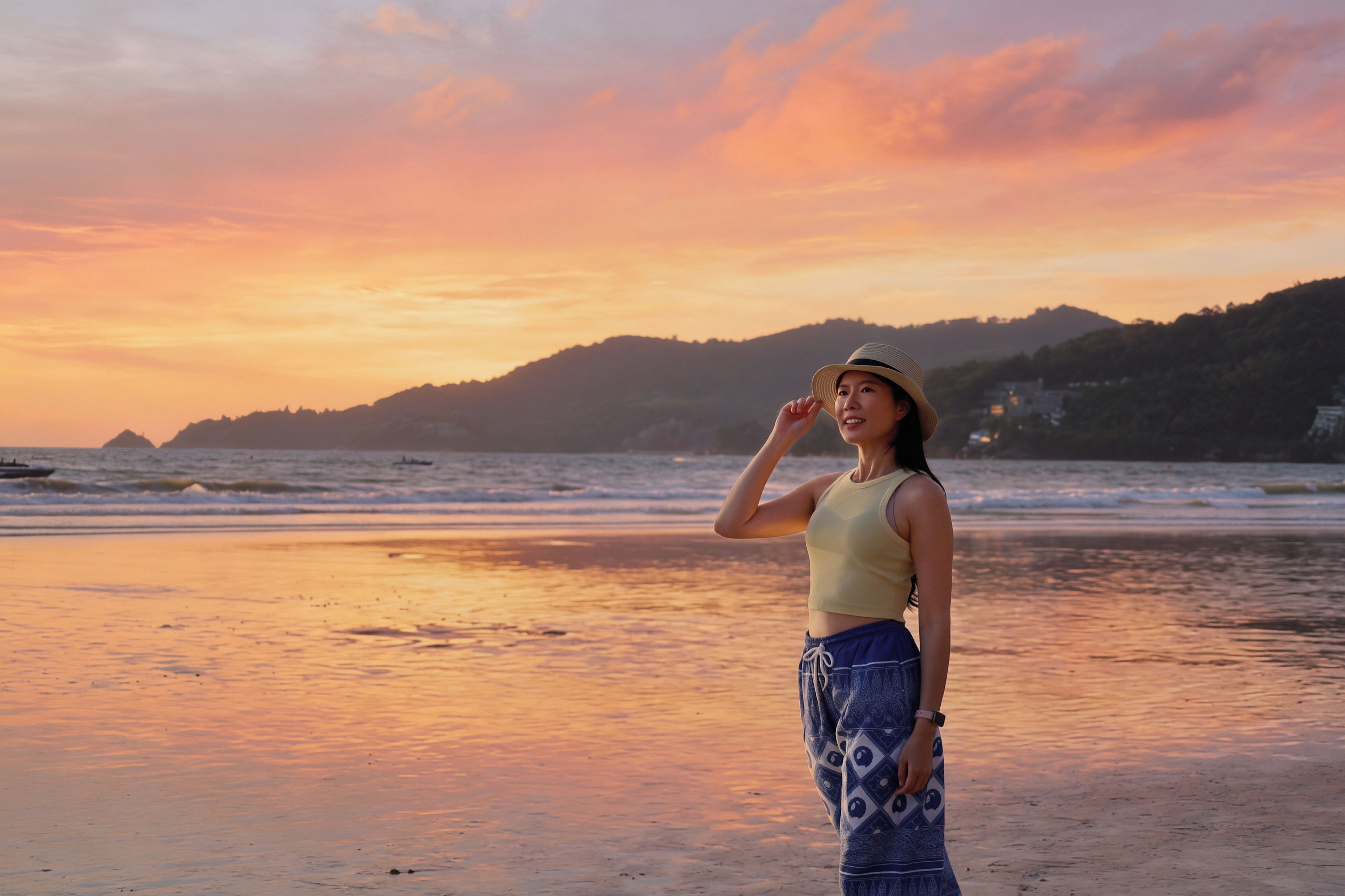 Une personne se tient sur une plage, avec un coucher de soleil en arrière-plan.
