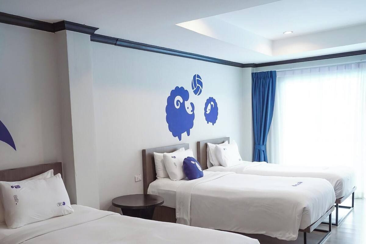A hotel room with two beds, a round table, and a wall with blue decorative elements.