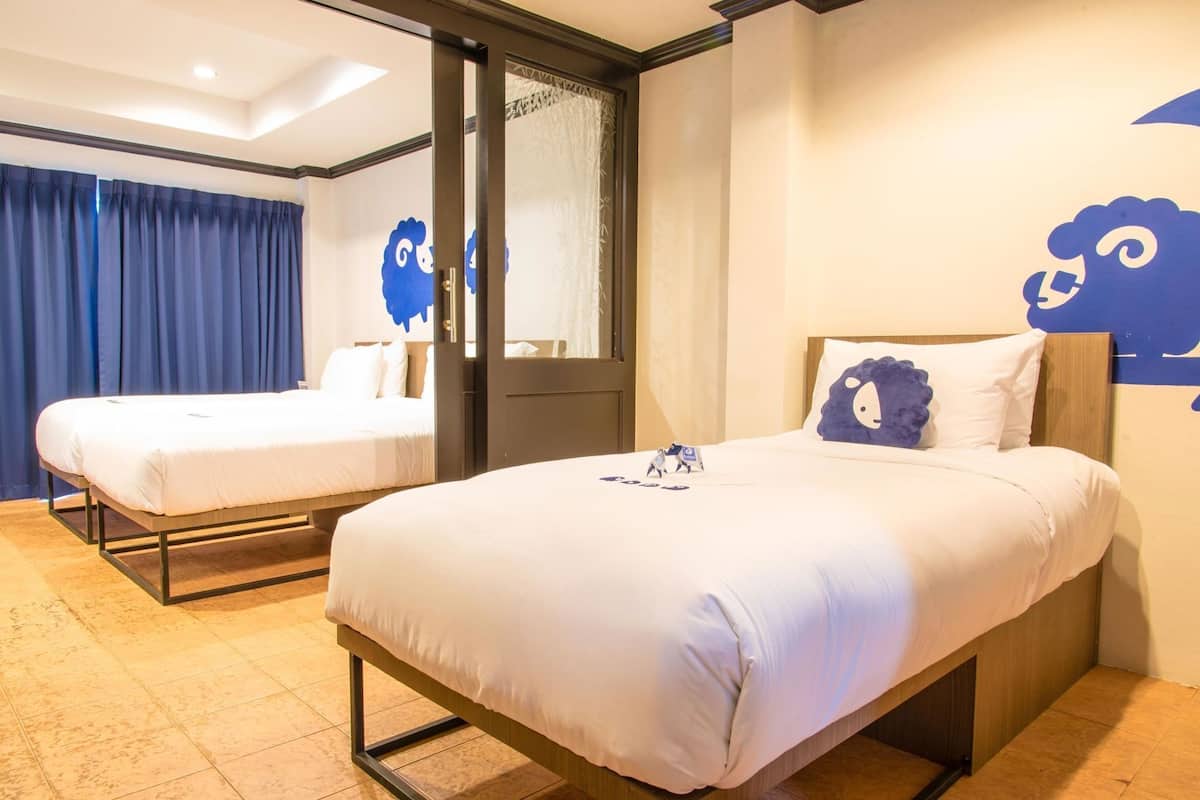 A hotel room with two beds, a door, and a wall with a sheep design.