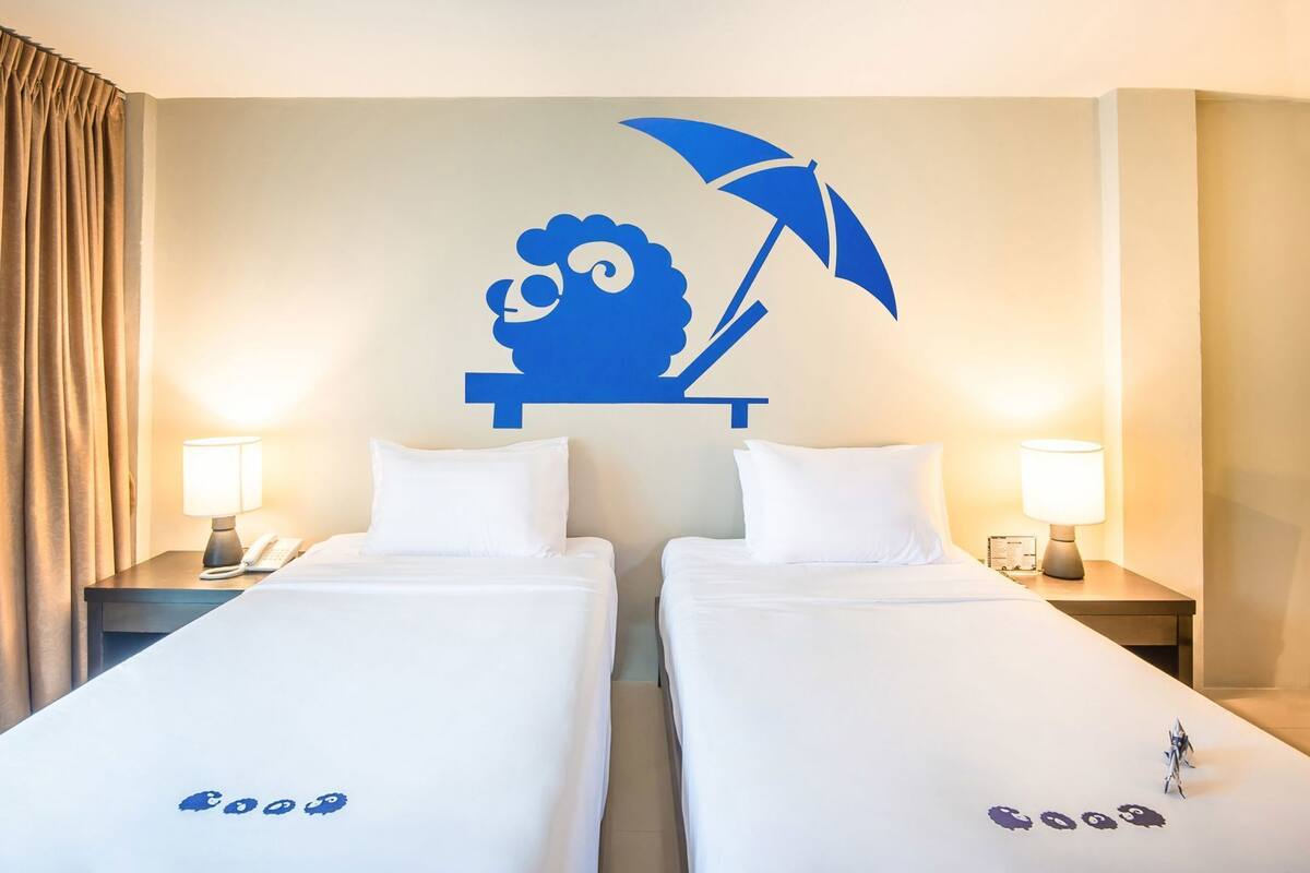 A hotel room with two beds, a wall decoration of a cartoon character with an umbrella, and bedside lamps.