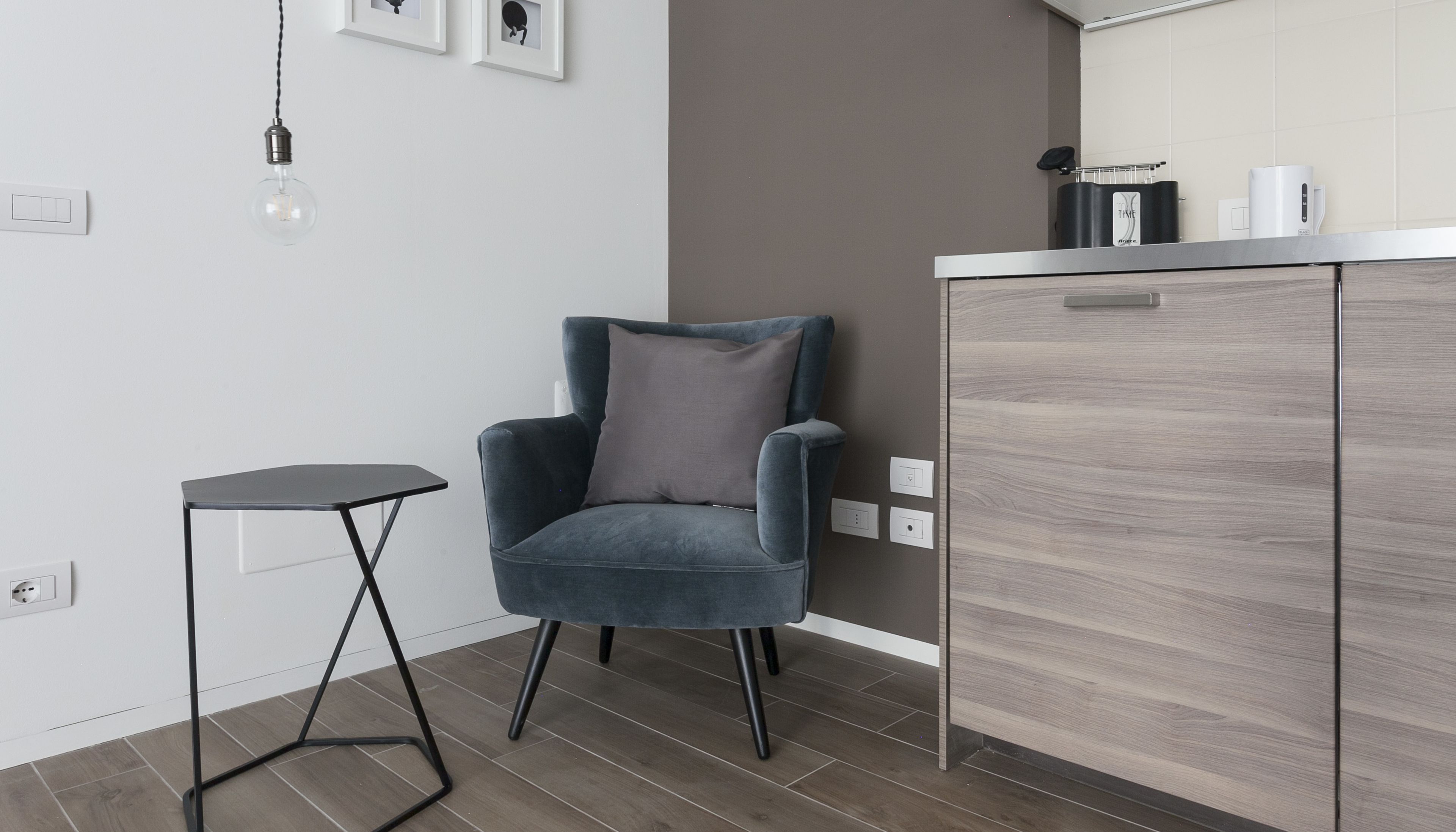 A modern kitchen with a grey cabinet, a small black side table, and a grey upholstered chair.