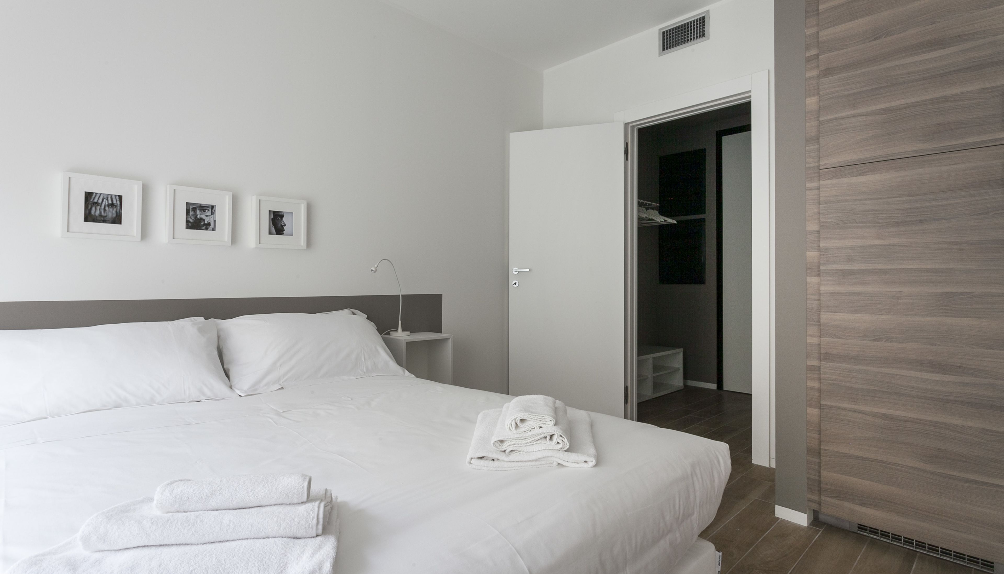 A modern hotel room with a large bed, a bedside table, a wardrobe, and a walk-in closet.
