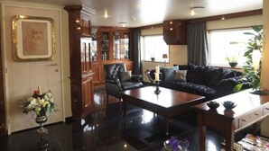 A spacious living area with a dark-colored sofa, a wooden coffee table, and a fireplace. There is a large window providing natural light and a view of the outdoors. - Crossgates Hotelship Nizzaufer - Frankfurt (Frankfurt)