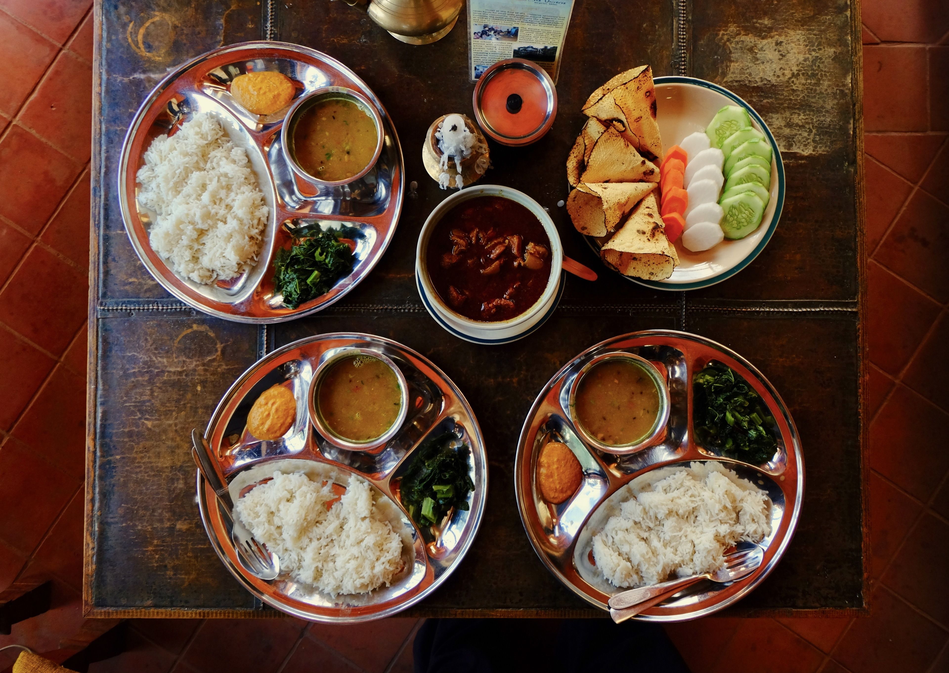 Una mesa con múltiples bandejas metálicas que contienen diversos platos, incluyendo arroz, verduras y guisos.