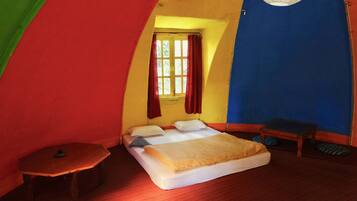 Una habitación pequeña y de forma peculiar con una cama, una mesita y un ventanal con cortinas.