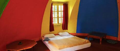A small, uniquely shaped room with a bed, a small table, and a window with curtains.