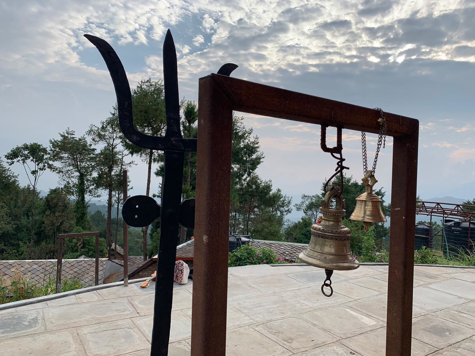 A metal structure with a bell hanging from it, set against a cloudy sky.