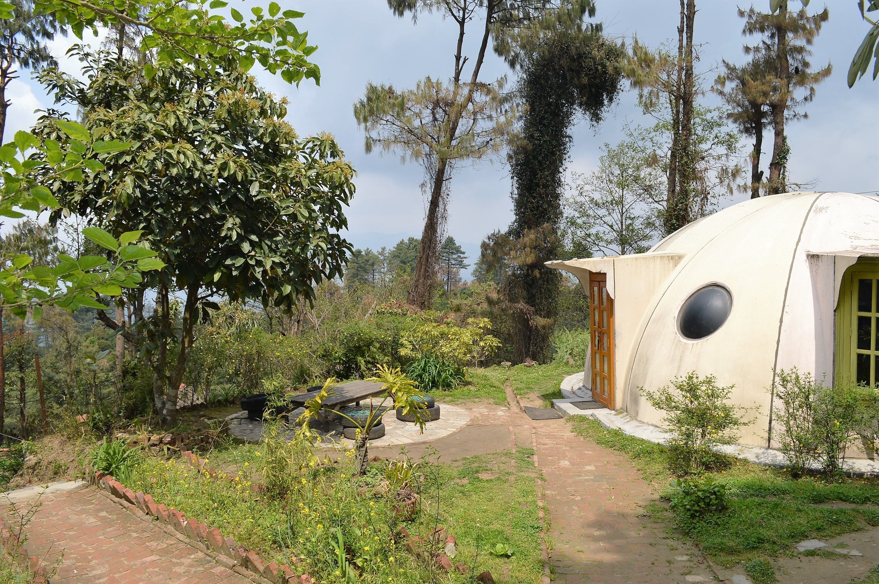 Un edificio con forma de cúpula y una ventana circular, rodeado de un jardín con diversas plantas y un sendero de ladrillos.